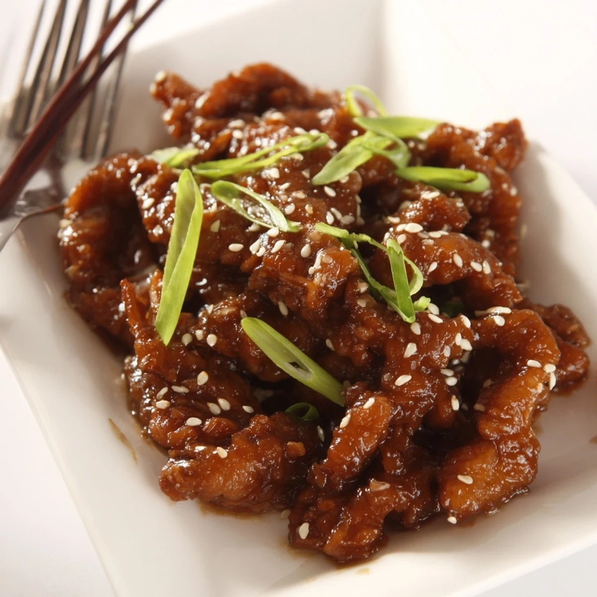 Tender shredded Crock Pot Sesame Chicken pieces drizzled with thick savory-sweet sesame glaze