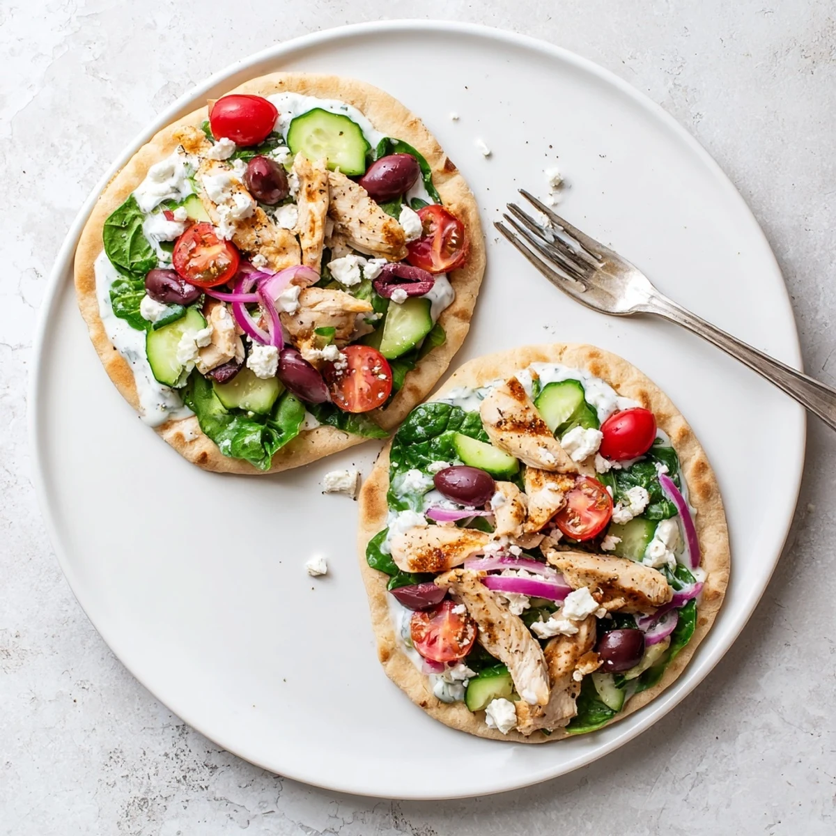 Savory Greek chicken flatbread loaded with fresh tomatoes cucumbers olives and crumbled feta cheese