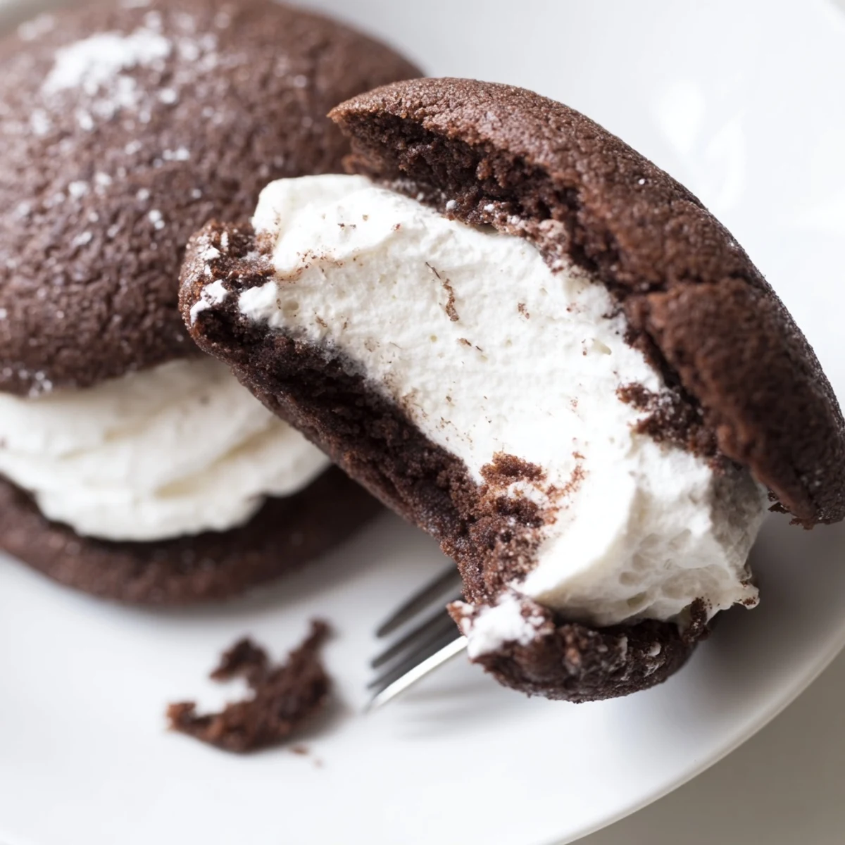 Two soft chocolate whoopie pies filled with fluffy white marshmallow cream on a white plate