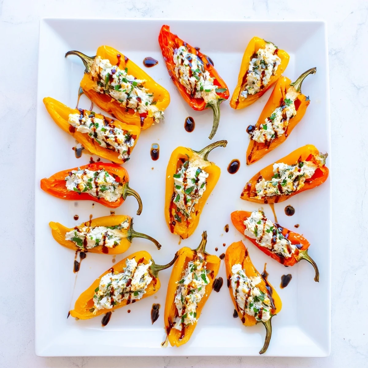 Mediterranean style roasted goat cheese stuffed mini peppers arranged on a baking sheet with balsamic glaze