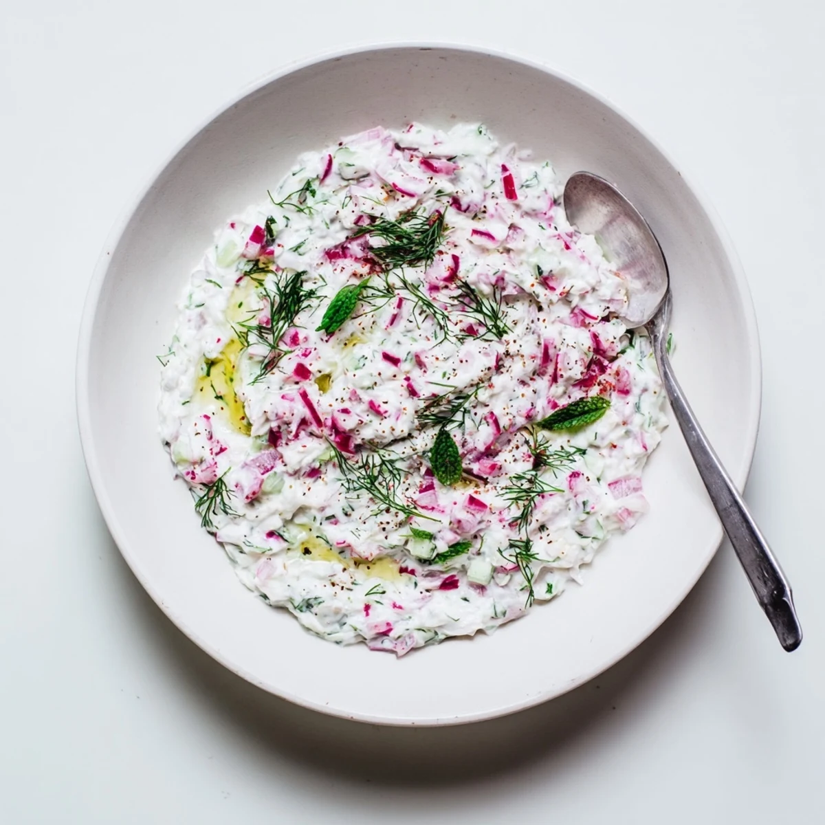White bowl of healthy radish tzatziki dip garnished with mint and olive oil drizzle on wooden board