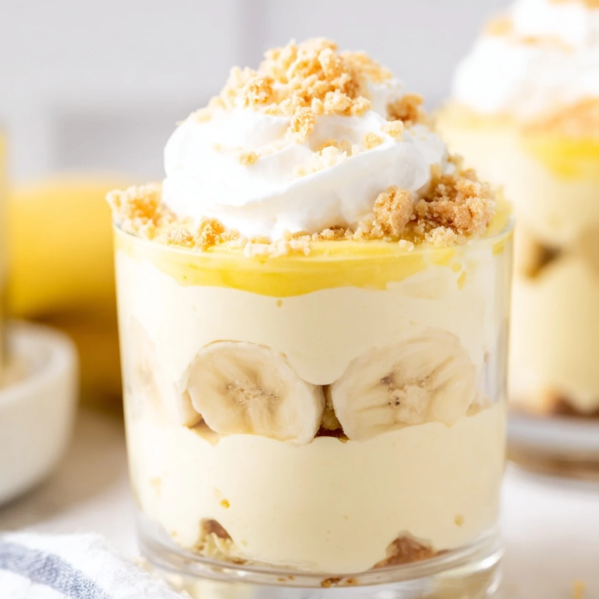 Individual no bake banana pudding cheesecake cups topped with golden wafer crumbs and whipped cream