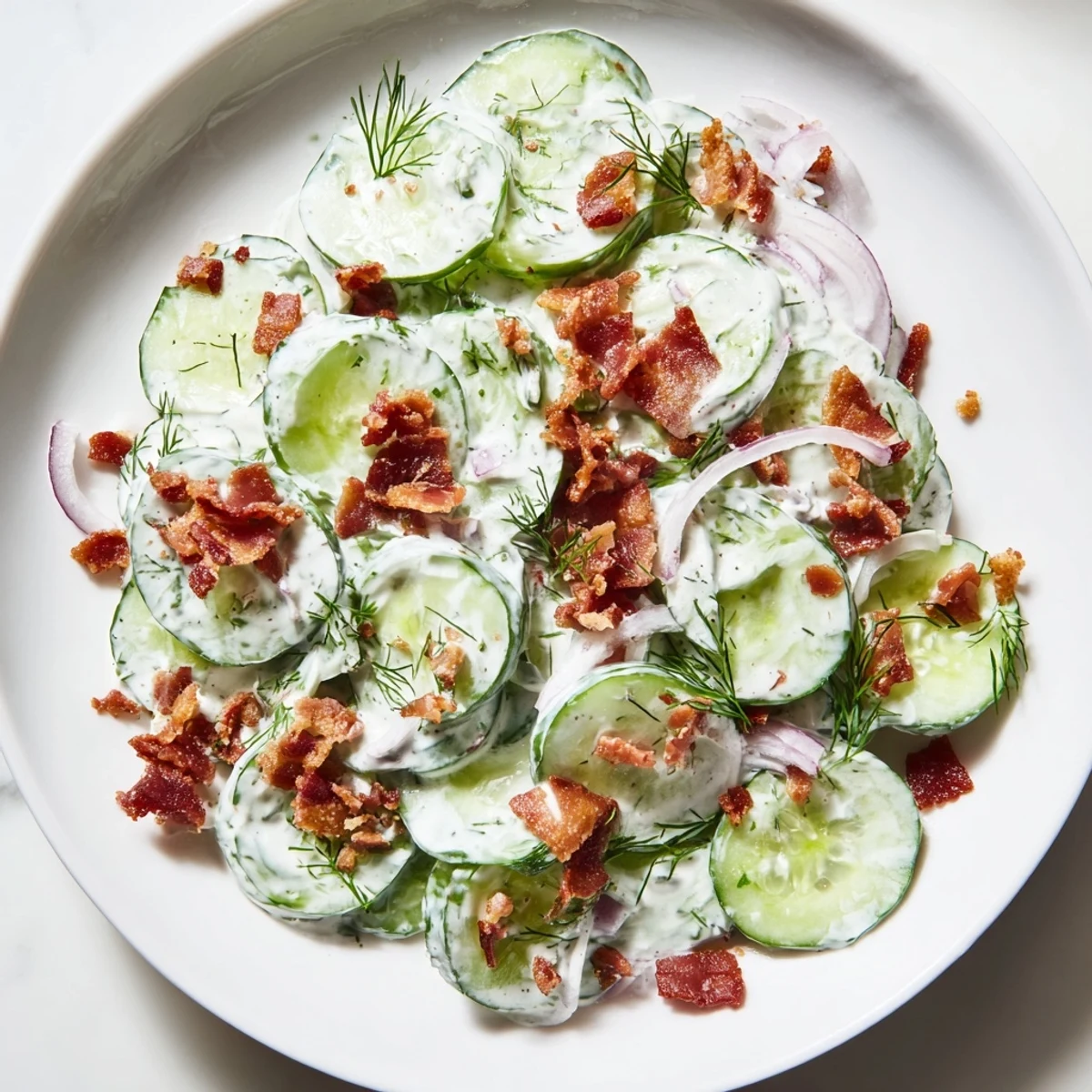 Crisp cucumber salad with bacon tossed in tangy Greek yogurt dressing on white plate