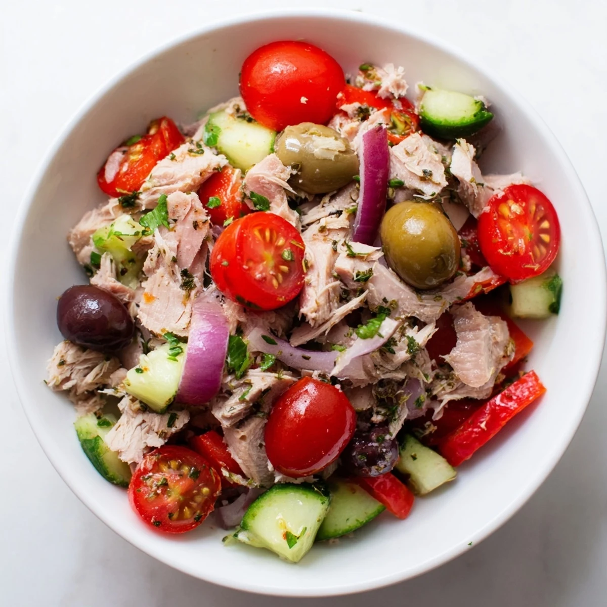 Mediterranean tuna salad in a white bowl with cherry tomatoes, olives, and fresh parsley