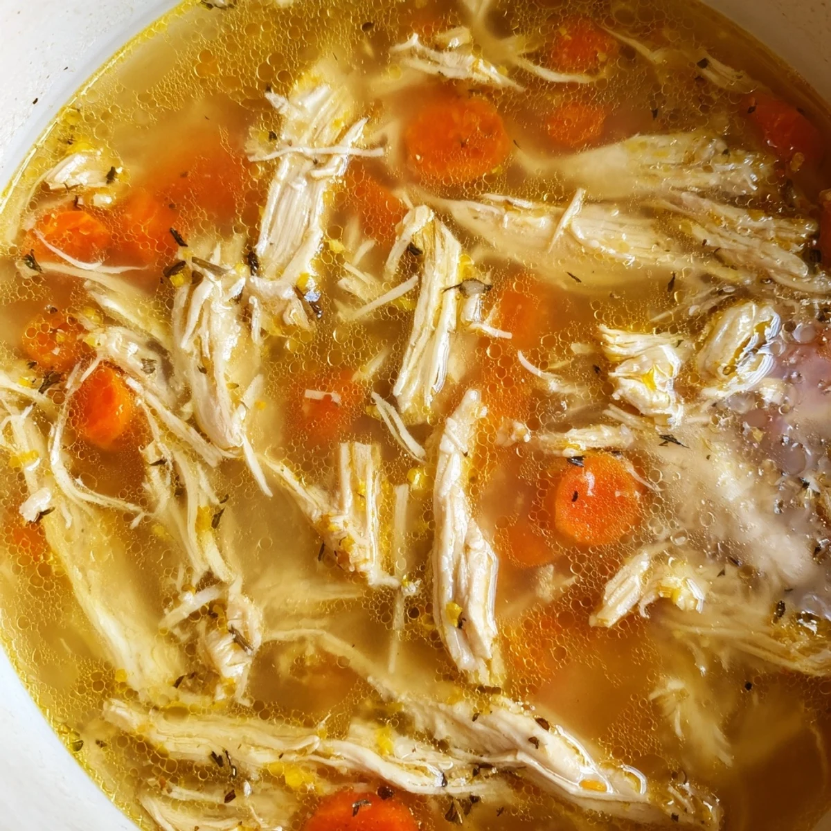 Golden Crockpot Lemon Chicken Soup with tender shredded meat and bright herbs in a white bowl