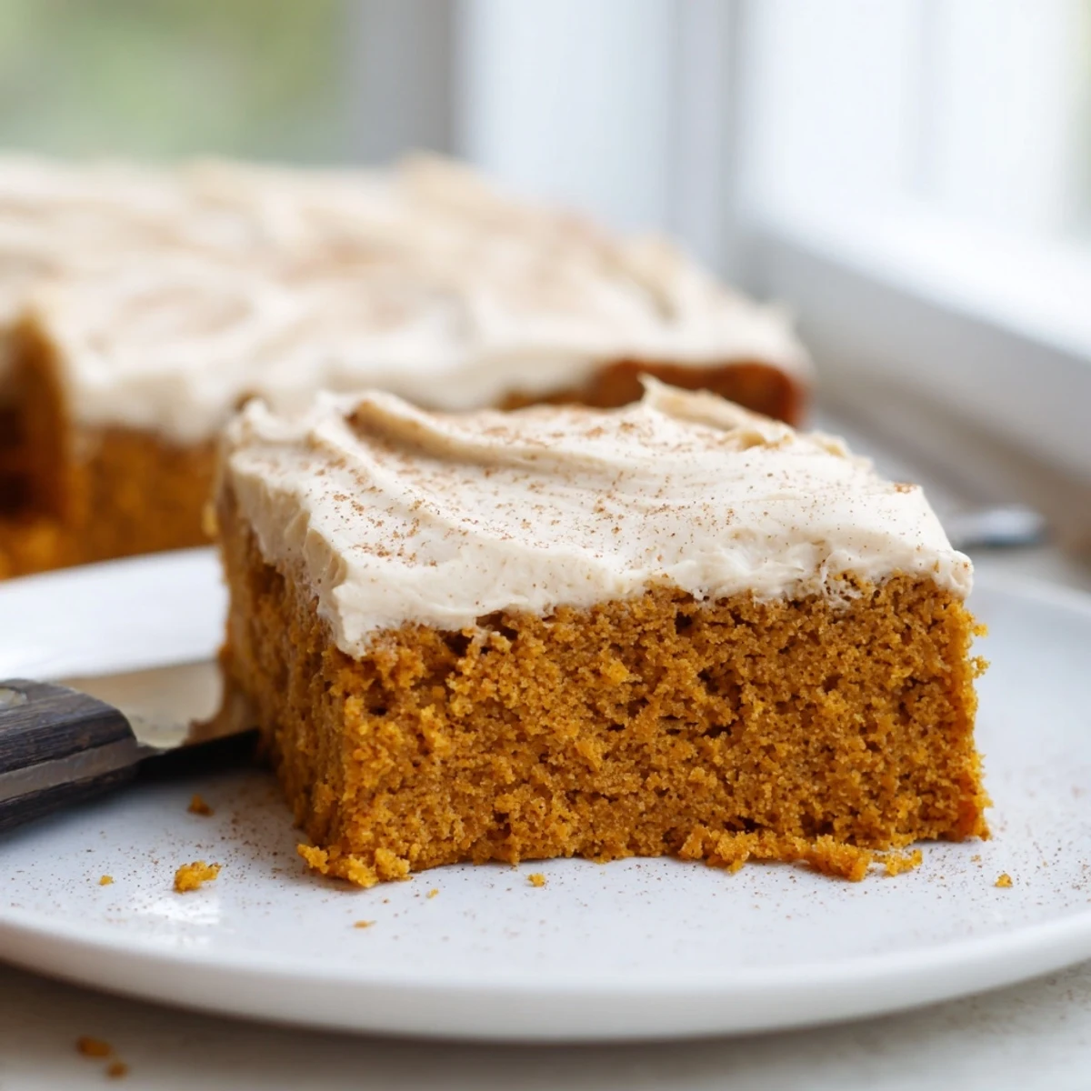 Thick pillowy cream cheese frosting spread over moist tender pumpkin bars in a baking pan