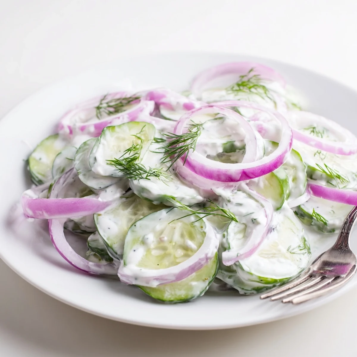 Fresh cucumber dill salad with thin slices and creamy dressing in white bowl