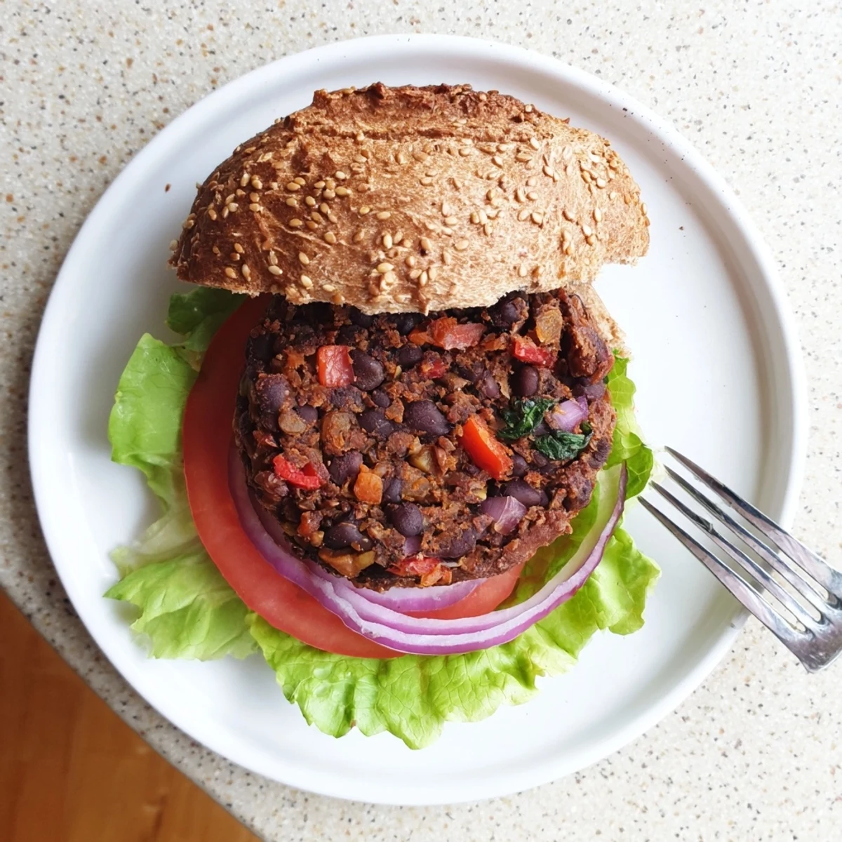 Golden brown veggie burger patty stacked on toasted bun with fresh lettuce tomato and creamy avocado slices