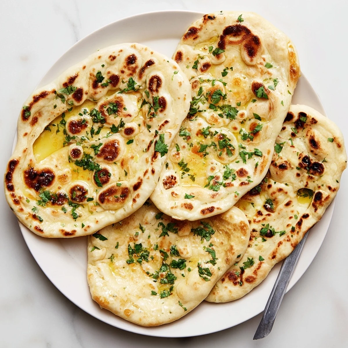 Handmade sourdough naan with garlic spots resting on a wooden serving board