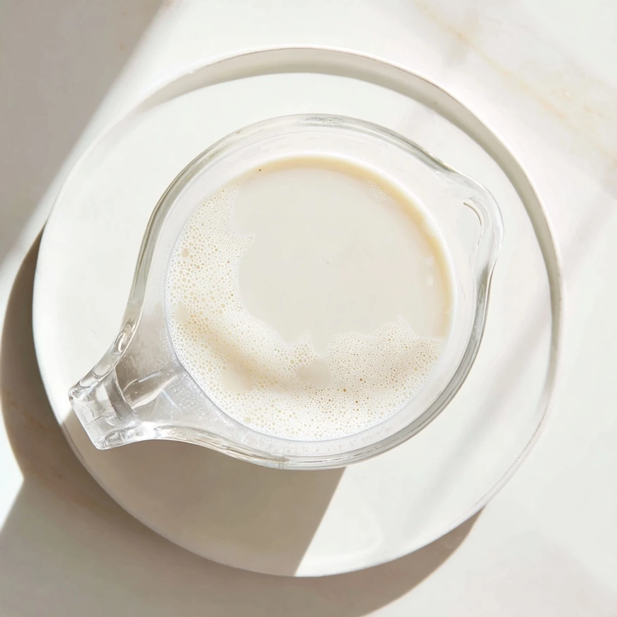 Glass of fresh almond milk on wooden table alongside raw almonds and vanilla extract ingredients