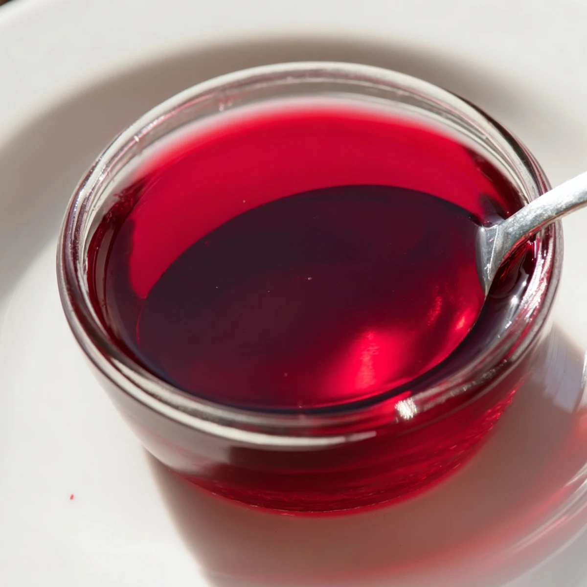 Glass jar of vibrant red cranberry syrup pouring onto stack of golden waffles